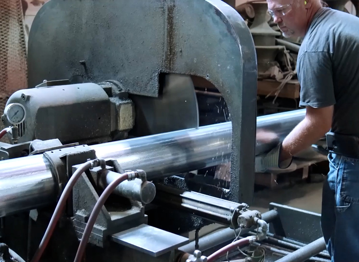 Operator holding aluminum pipe as it’s being cut to a specific length